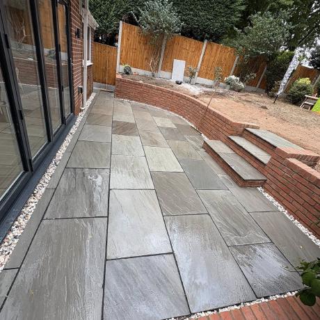 Grey Indian sandstone patio with curved brick retaining wall and steps